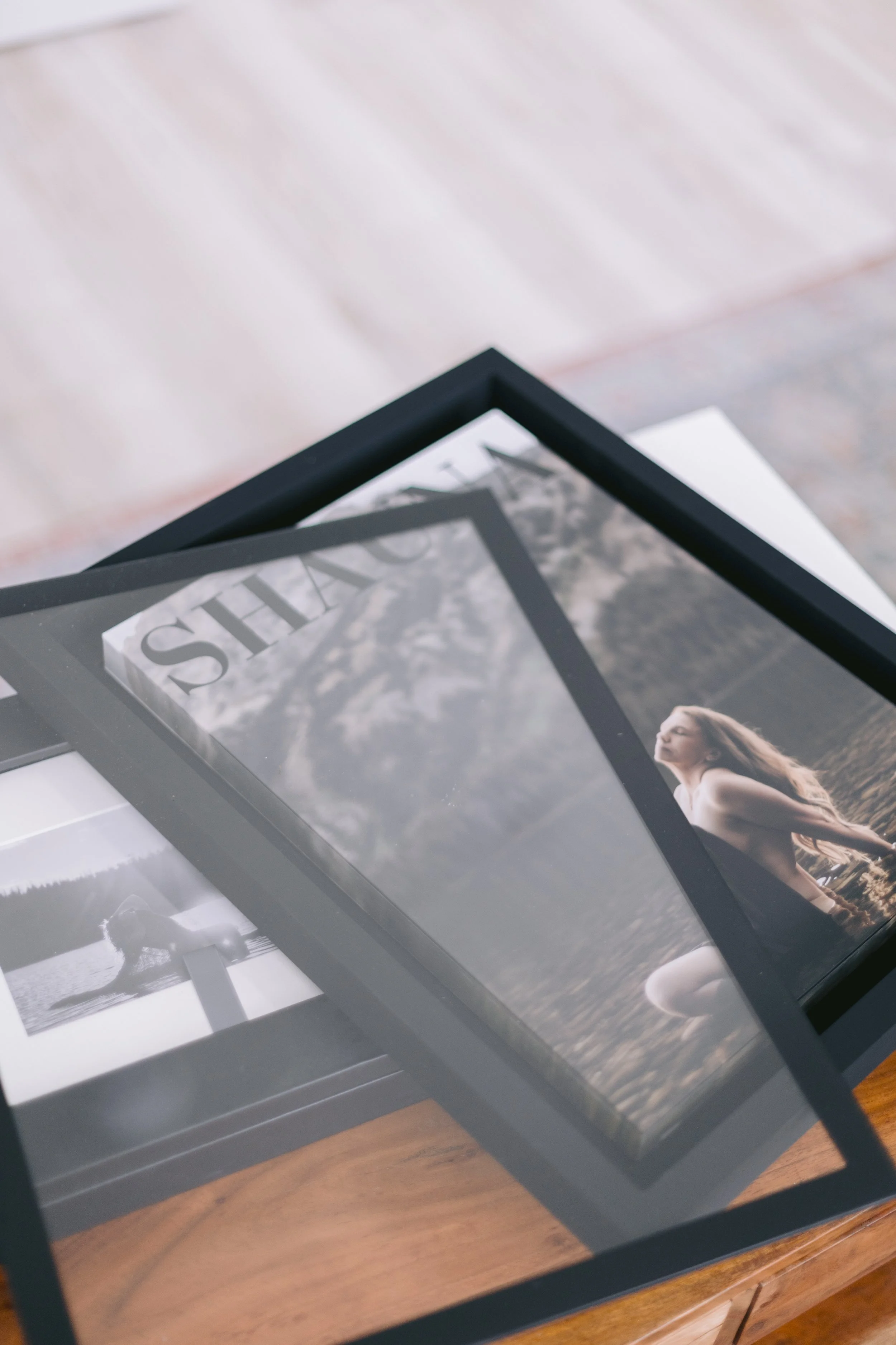 Framed photographs on a glass surface, featuring black-and-white images of a person walking on the beach and a woman in a field, with the focus on the corners of the frames and the reflections on the glass.