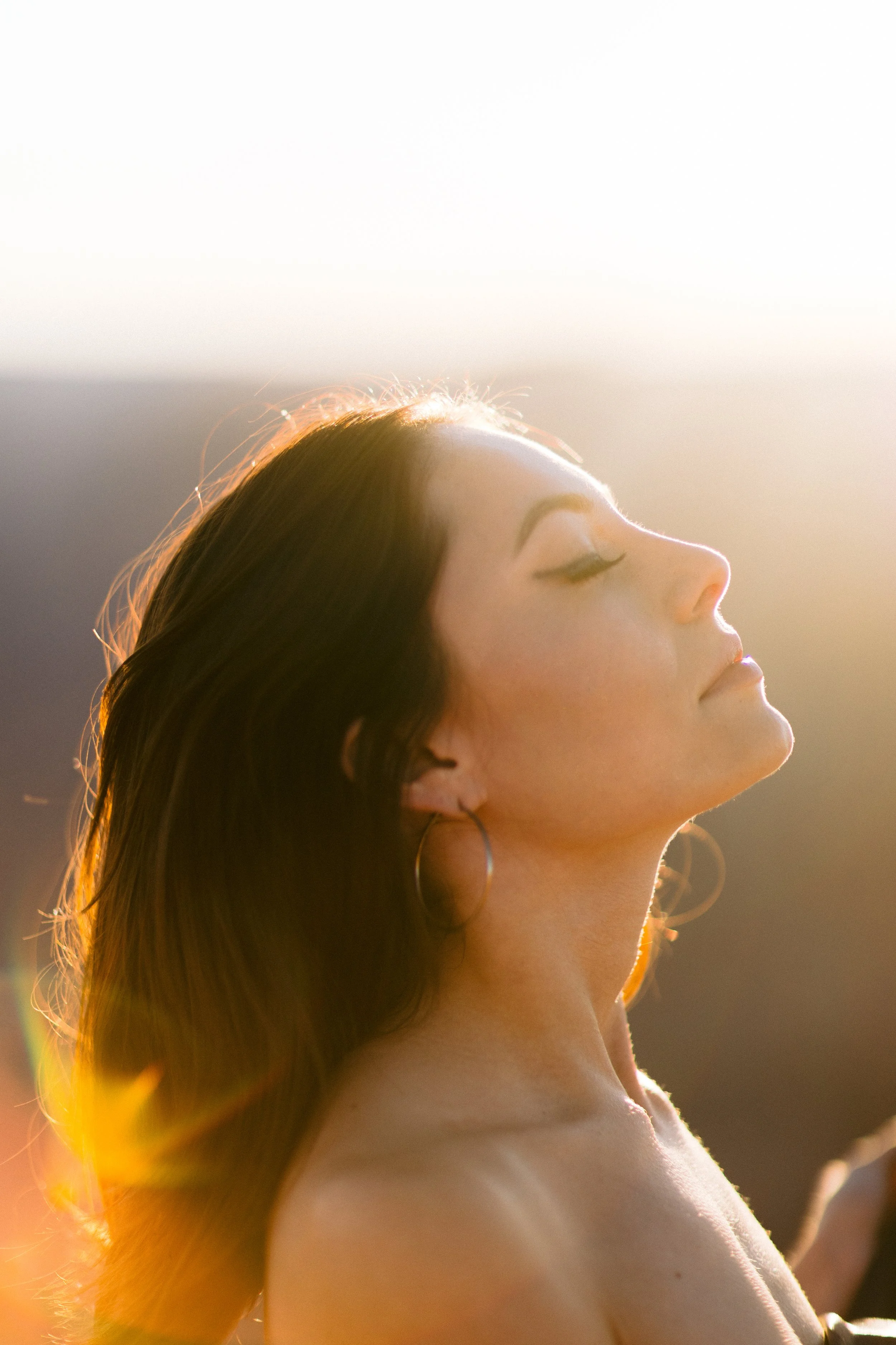 Close-up of a woman with eyes closed and long hair, illuminated by soft sunlight.