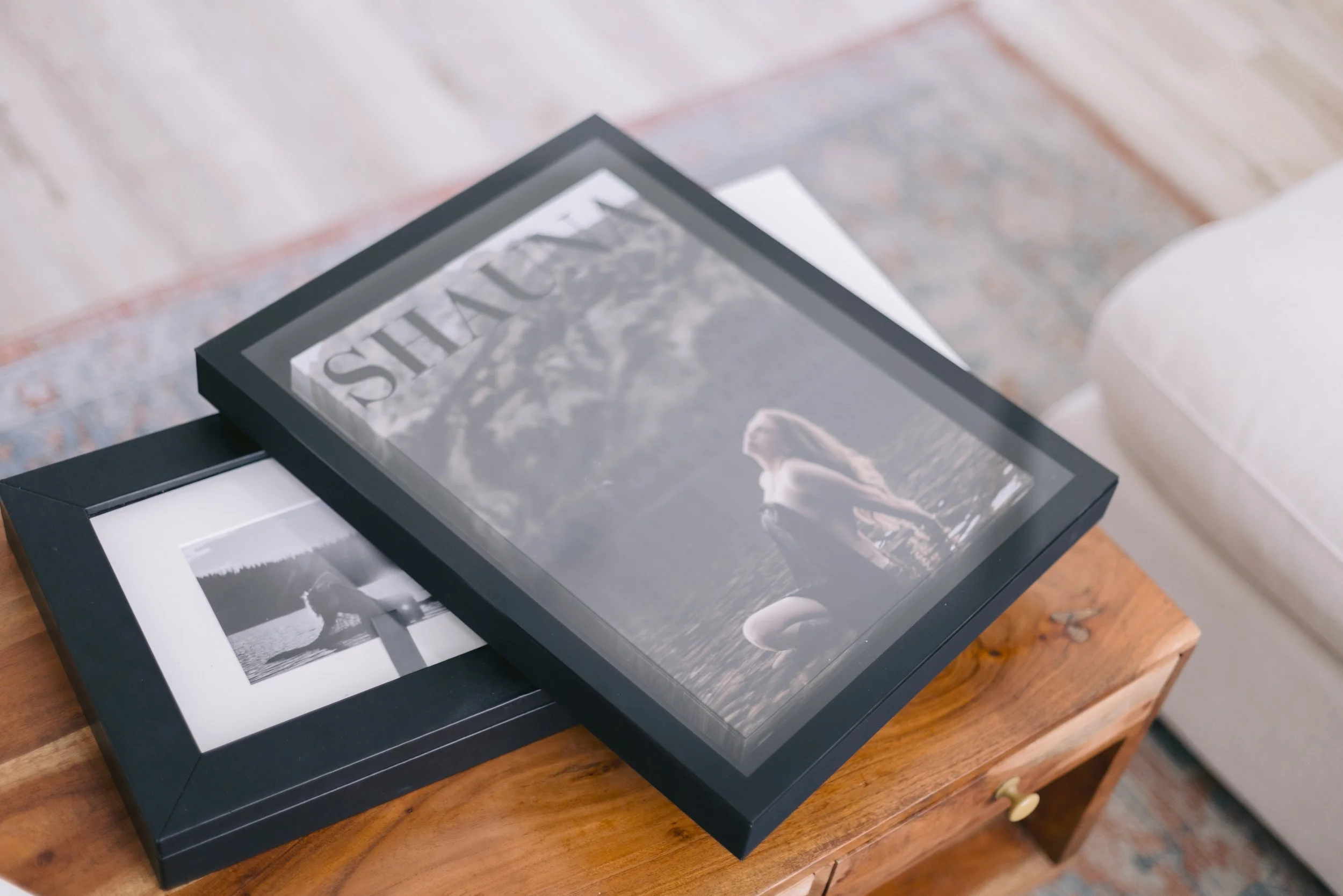 A collection of black and white photographs and art prints laid out on top of a black frame or box on a wooden surface.