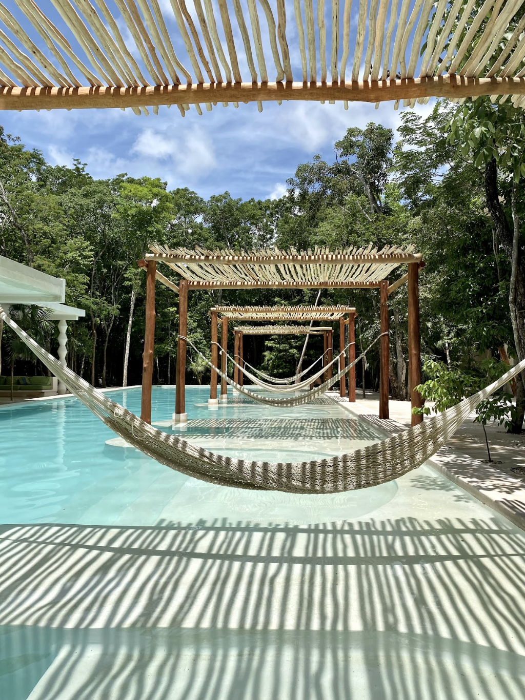 Hammocks hanging over a tropical swimming pool beneath a wooden pergola in a lush forest resort