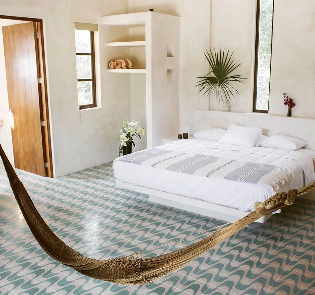 Bright minimalist bedroom with a white bed, patterned tile floor, built-in shelves, tropical plant, and suspended hammock.