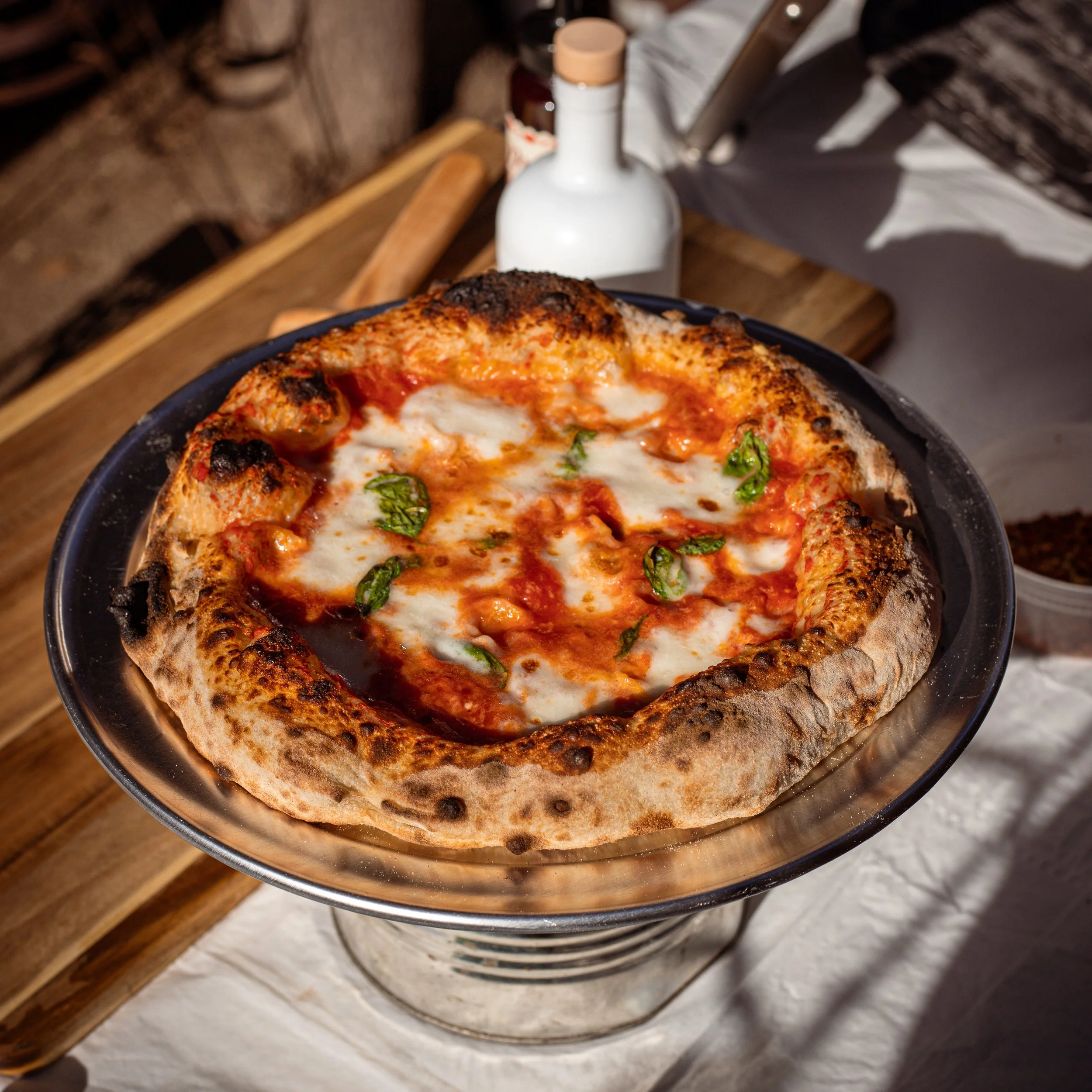 A close-up view of a pizza with cheese, tomato sauce, basil, and a thick, burnt crust in a black pizza pan.