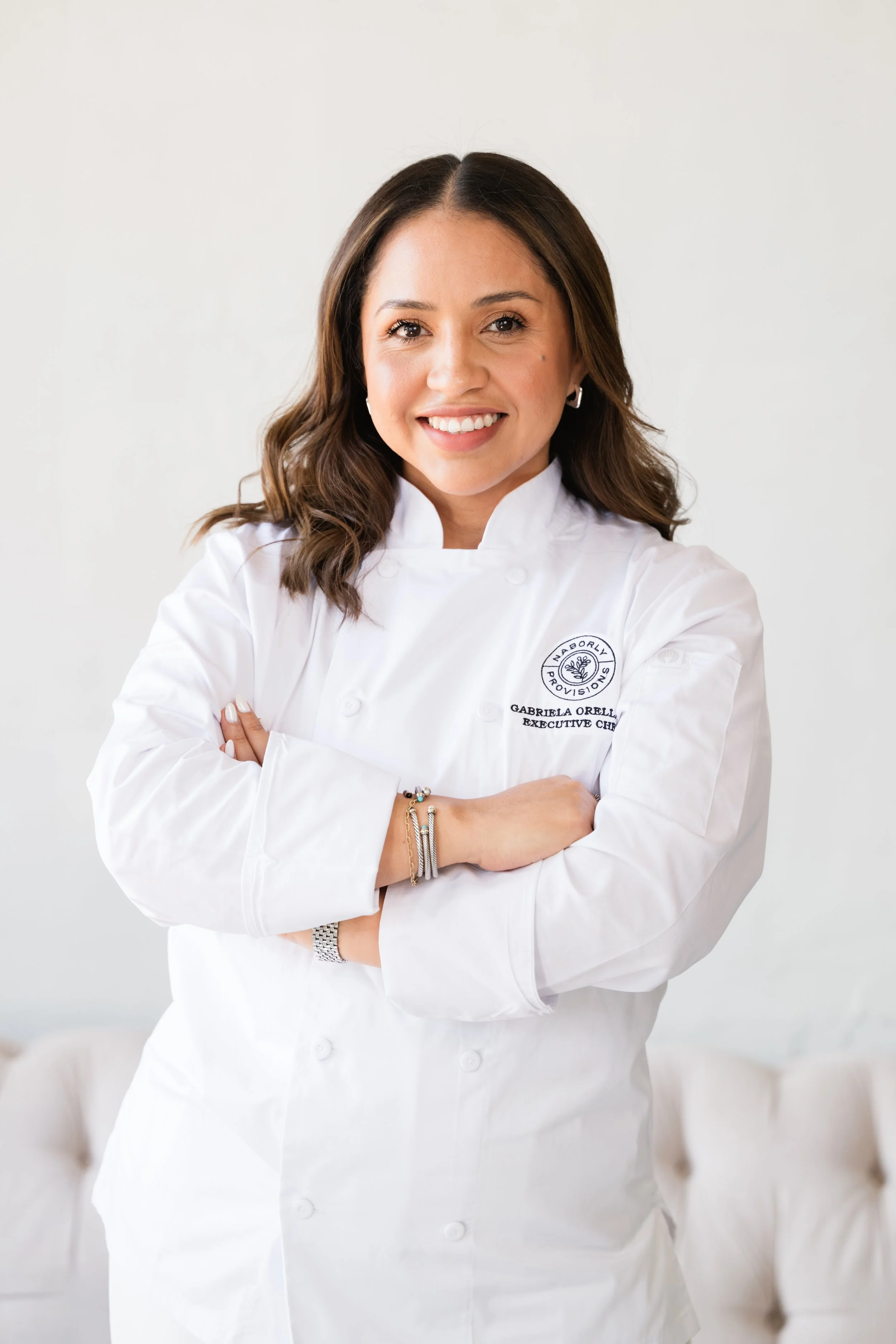 Woman sitting on a green chair, wearing a black suit, with a white paneled wall in the background.