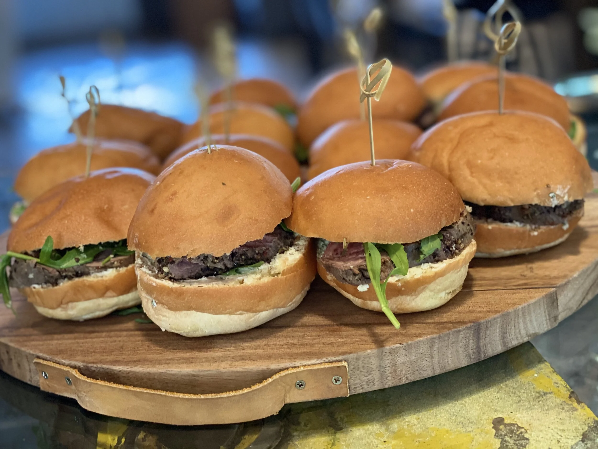 Mini burgers on a wooden platter with skewers