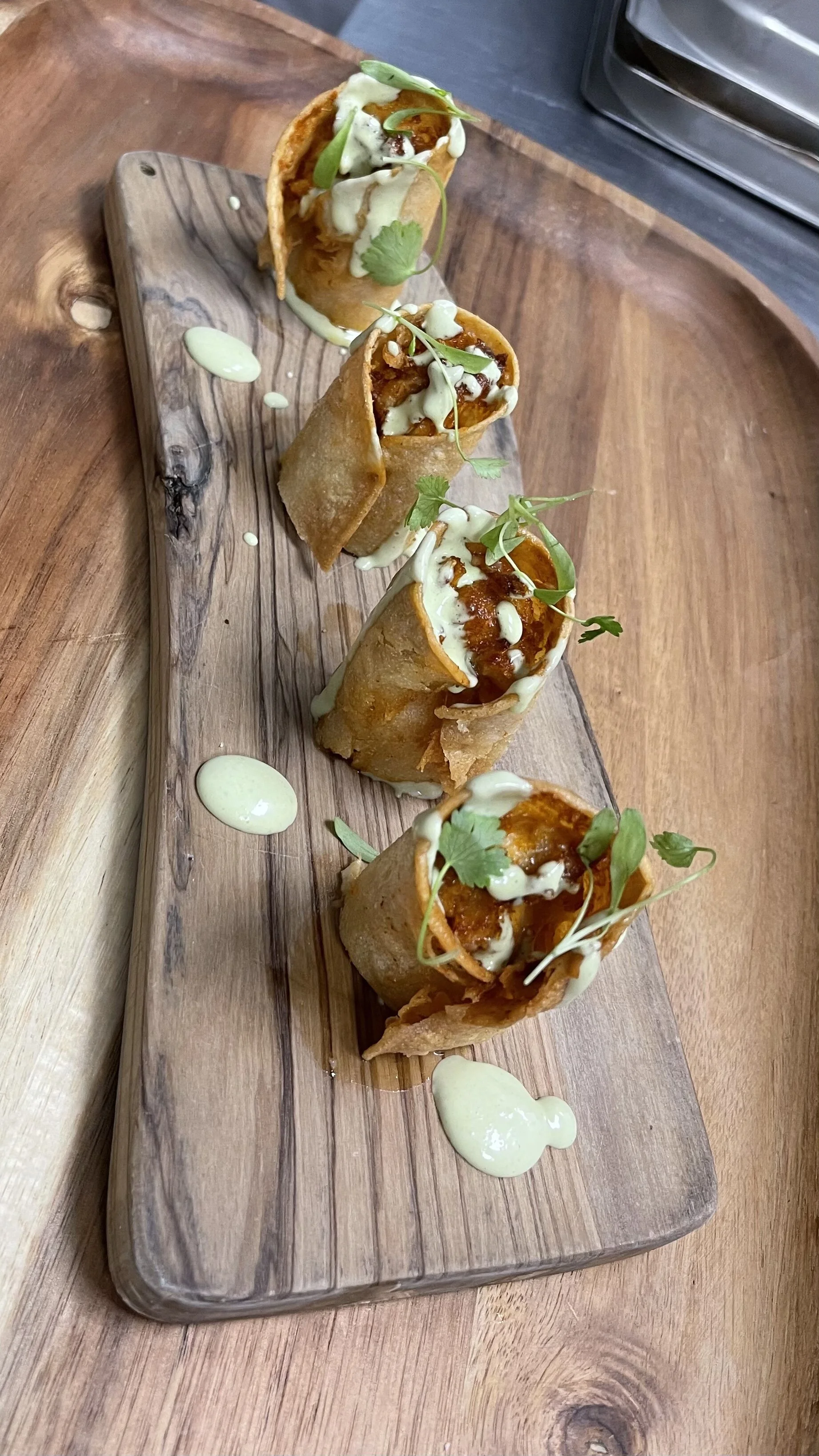 Gourmet rolled tacos with sauce on wooden board