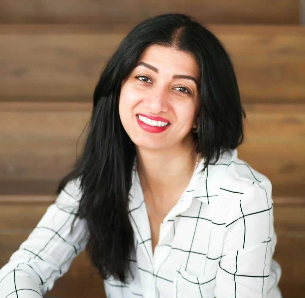 Jodi Rai is wearing a white check shirt and smiling as she looks at the camera.