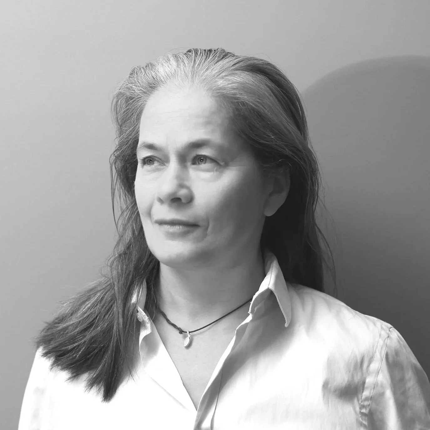 Zwart-wit foto van een oudere vrouw met lang, grijs haar die naar links kijkt, gekleed in een witte blouse en een kettinkje.