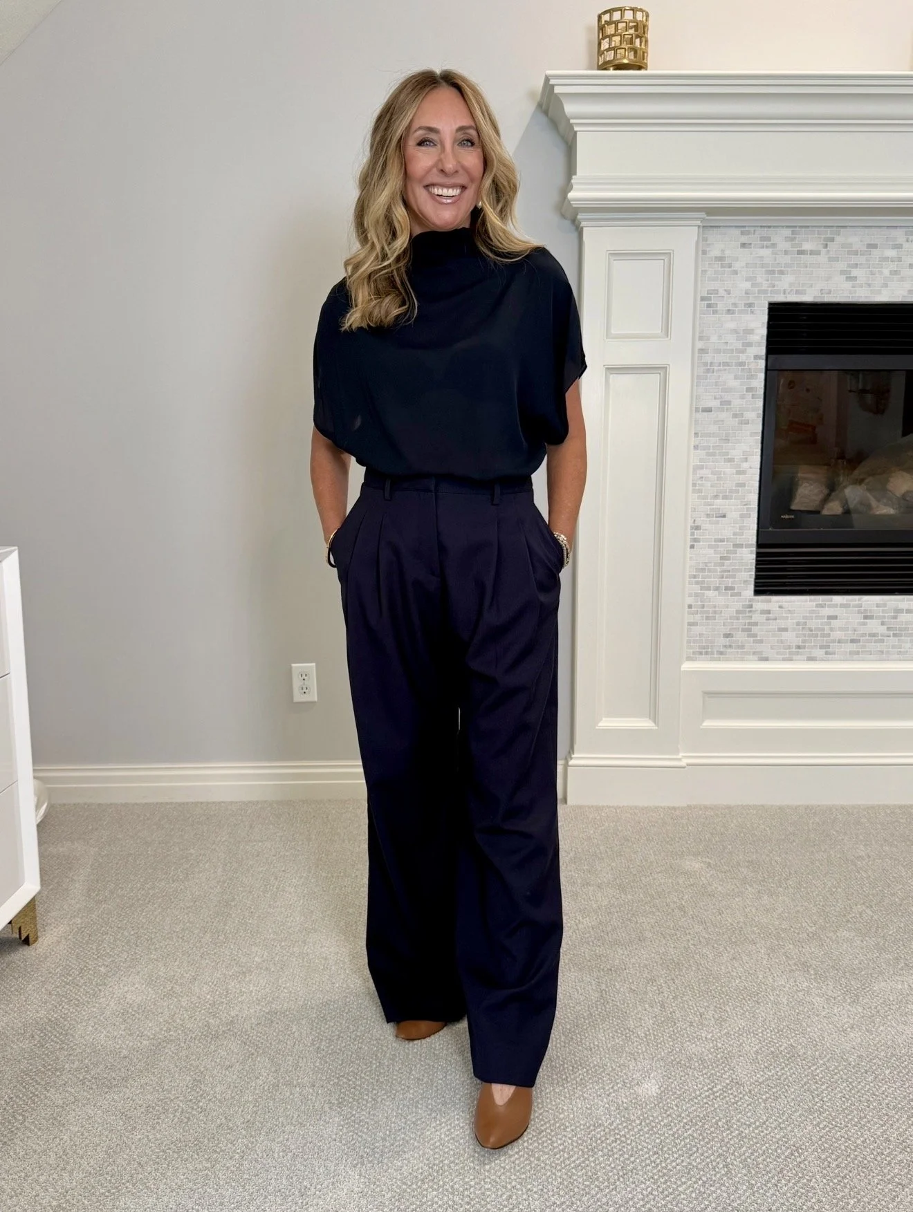 Hallie in the TWP navy mockneck cap sleeve top with navy pleated trousers and tan flats