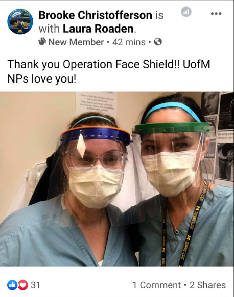 Two healthcare workers wearing face masks, face shields, and scrubs taking a selfie in a medical setting.