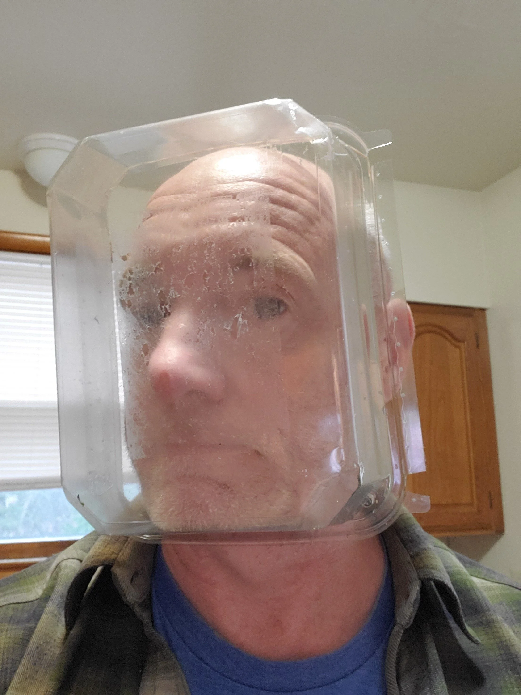 A man with a plastic container on his head, pressing against his face, creating a distorted view of his face through the plastic.