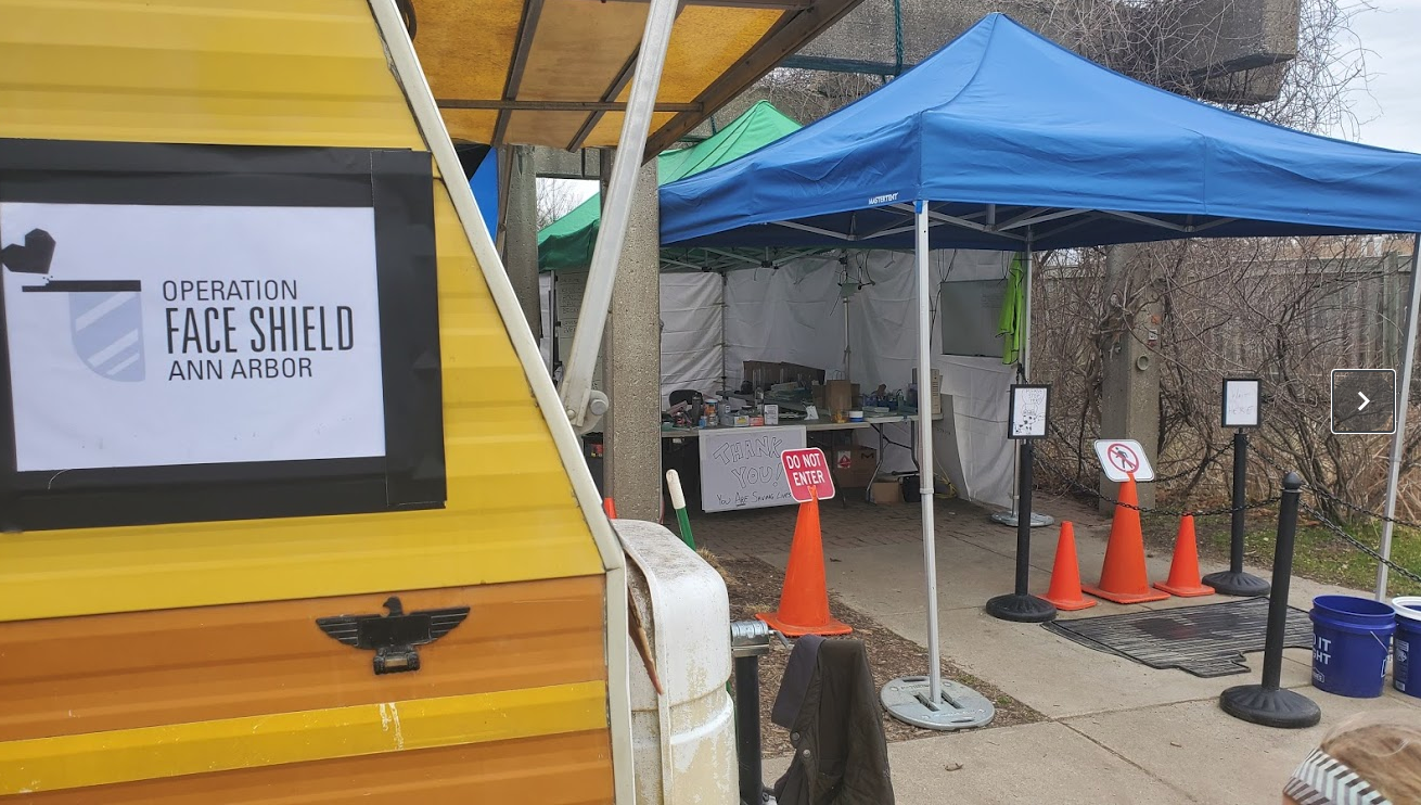 Outdoor setup with tents, orange cones, and signs for Face Shield Operation in Ann Arbor, with a food truck on the side.