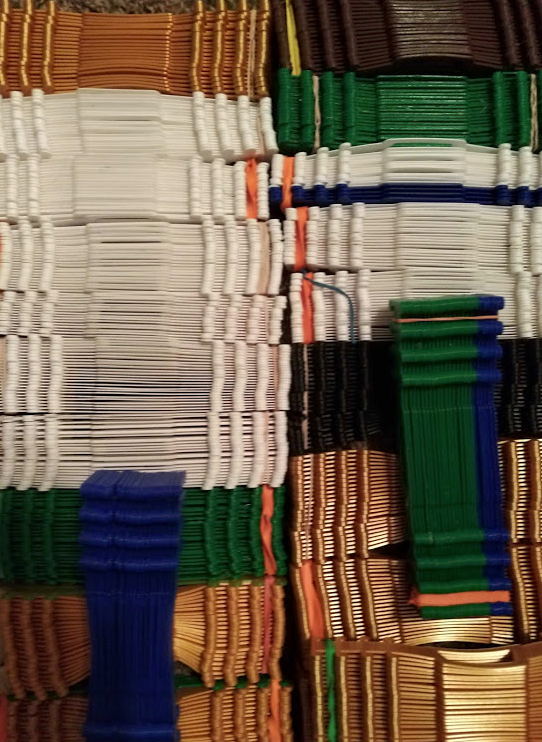 A colorful collection of woven plastic or possibly rubber strips arranged in rows of various colors including white, green, black, blue, orange, and brown.