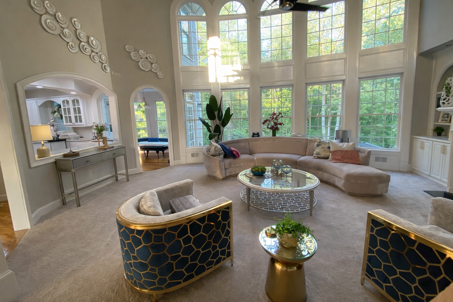 Luxury sitting room with navy and gold geometric accent chairs, curved sectional sofa, and floor to ceiling windows in a Hoschton Georgia home designed by Welcome Home Interiors