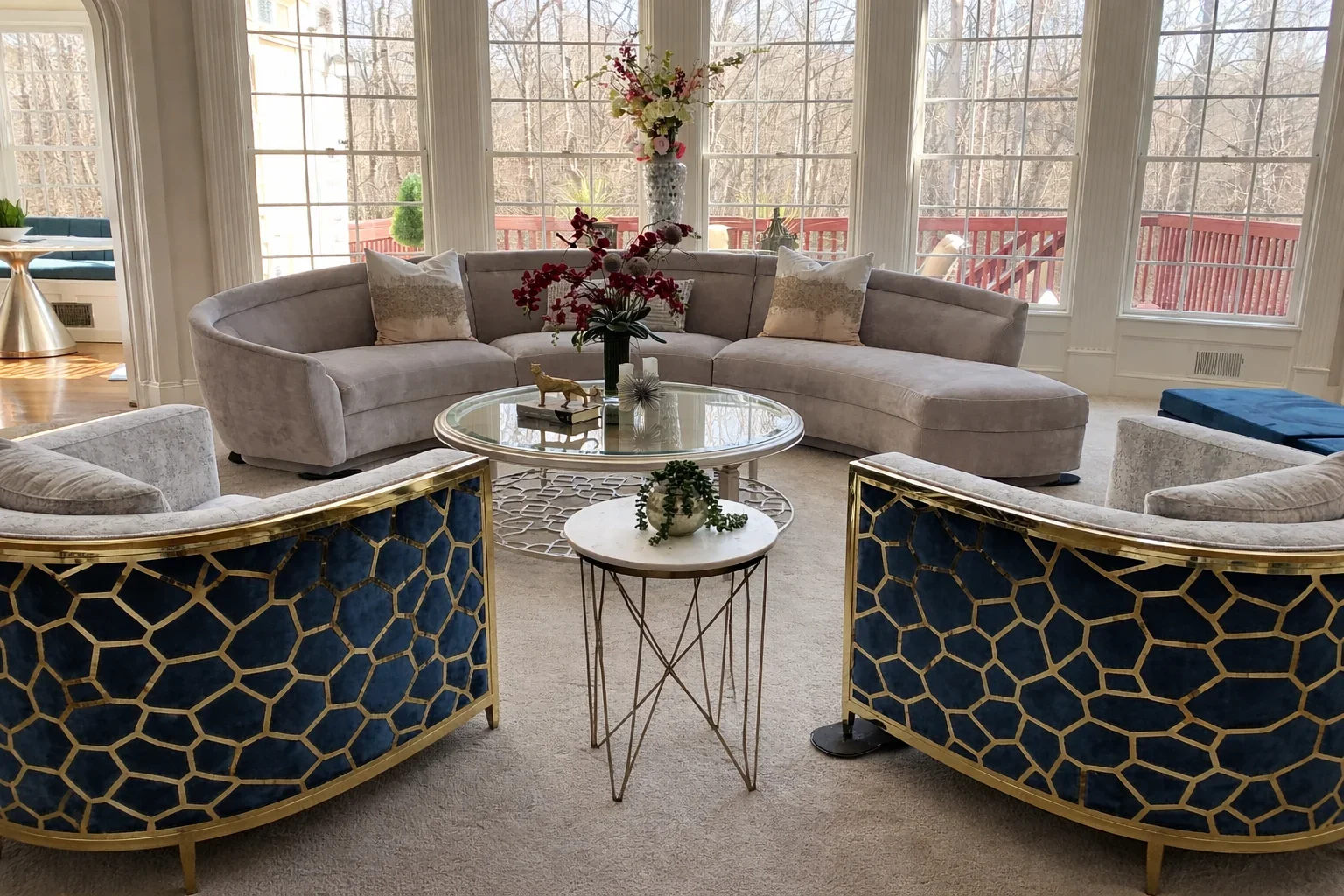 Elegant living room with a curved sectional, glass coffee table, and blue accent chairs, styled for a refined residential interior.
