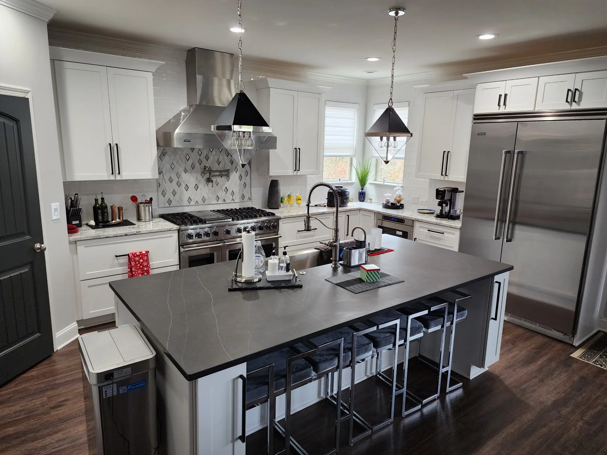 Modern kitchen with white cabinets, stainless steel appliances, a black kitchen island with bar stools, pendant lighting, and wooden flooring.