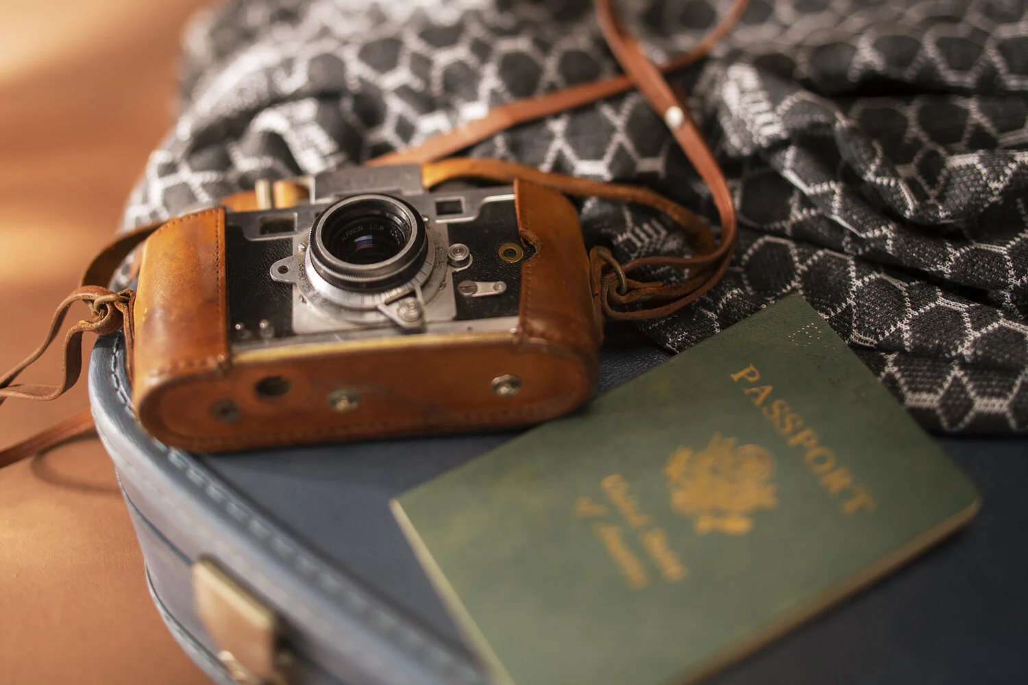 A vintage camera in a leather case, a green passport, and a black patterned scarf on a dark suit jacket.