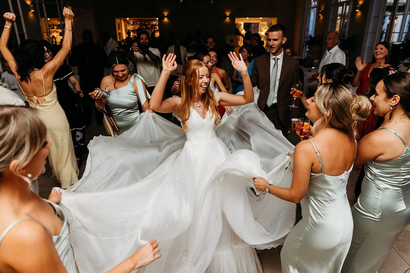 Bride in white wedding dress dancing joyfully with friends and guests at her wedding reception.