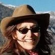 Woman wearing sunglasses and a wide-brimmed hat, smiling outdoors with a blue sky background.
