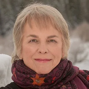 Close-up of a woman outdoors in winter, wearing a scarf with a snowy background.