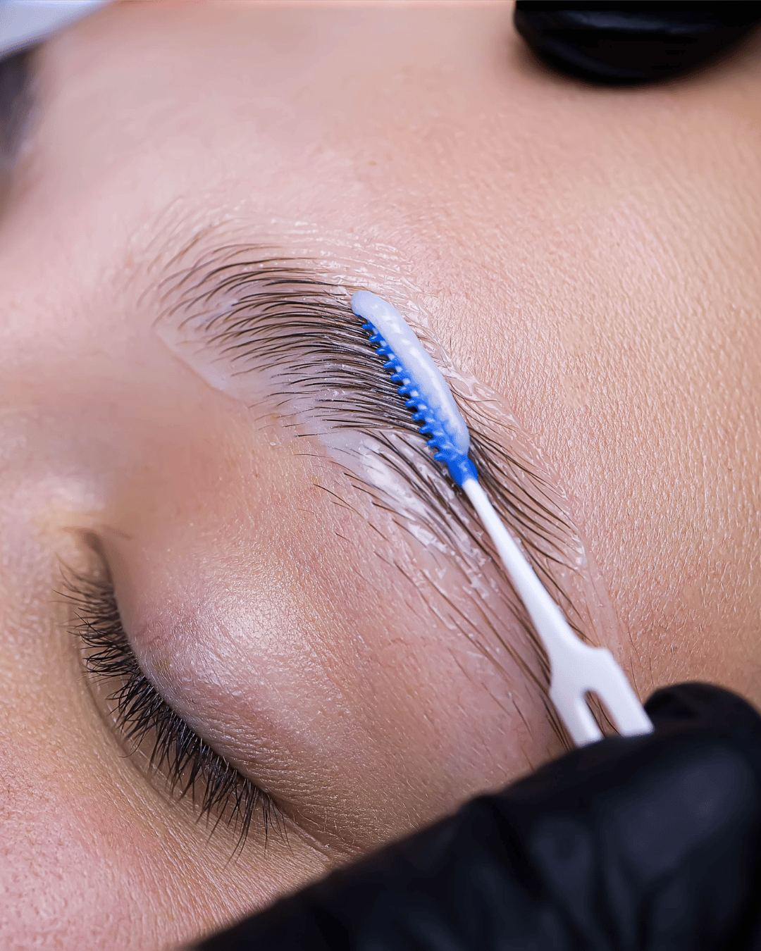 Close-up of an eye with an eyelash brush applying cleaning solution to the eyelashes.
