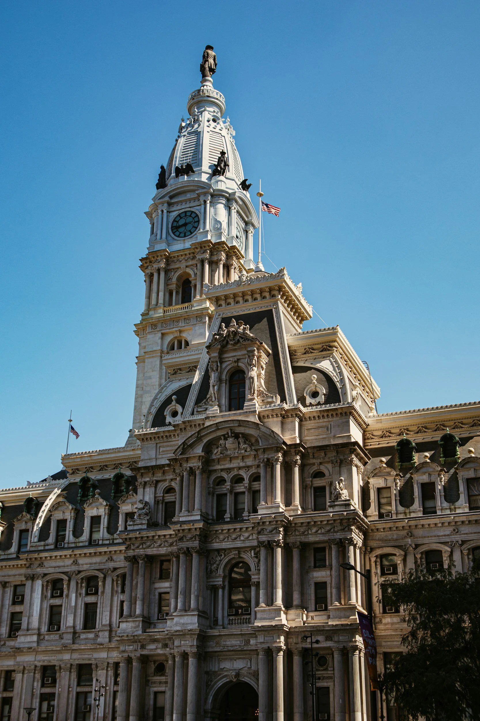 Philadelphia City Hall with its ornate stone facade, clock tower, and statue atop the spire, against a clear blue sky.