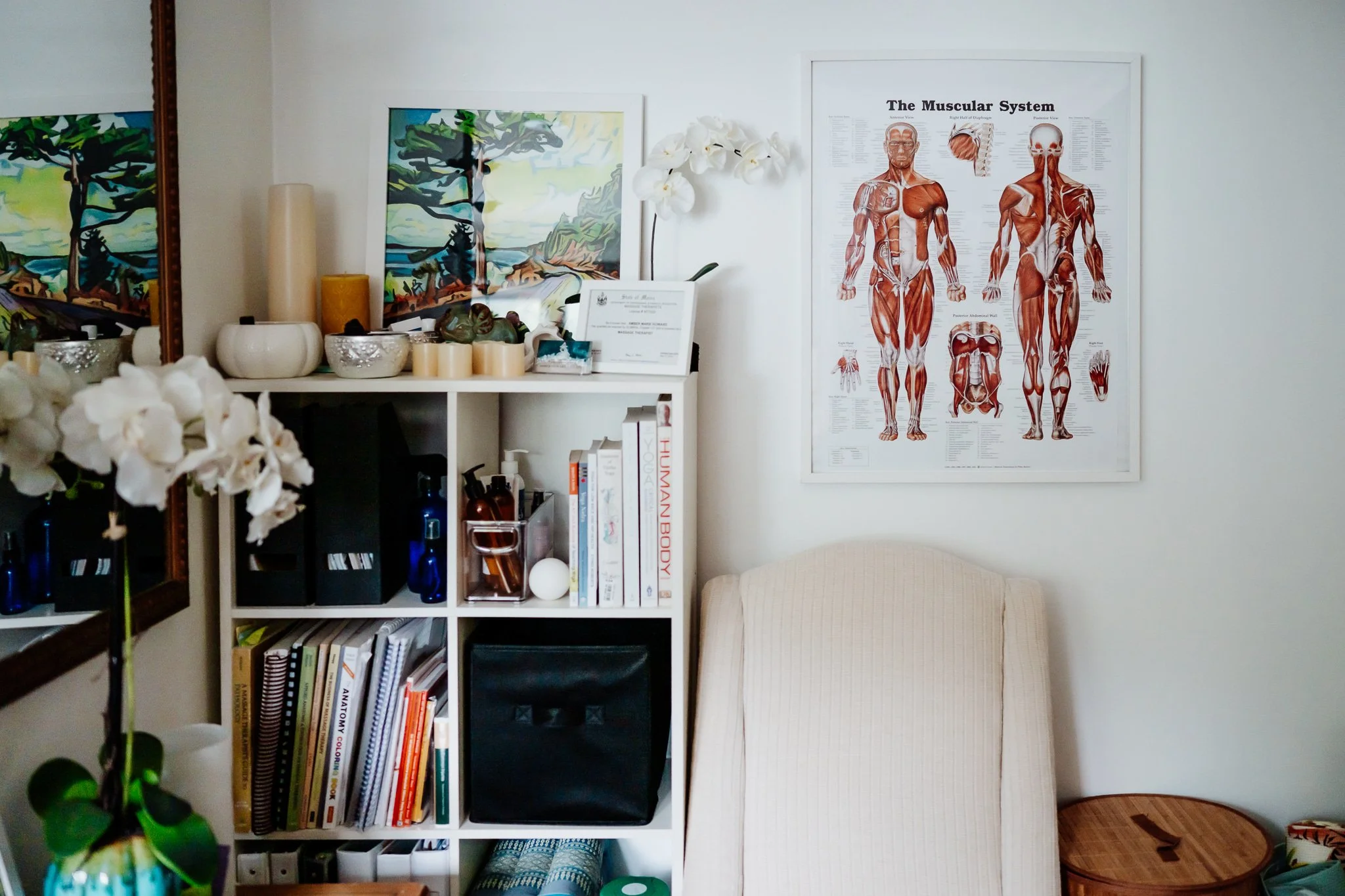 Therapeutic massage office in Bar Harbor, Maine with medical massage poster, Maine artwork, and a bookshelf filled with anatomy and kinesiology textbooks, massage lotions, aromatherapy supplies and bodywork tools