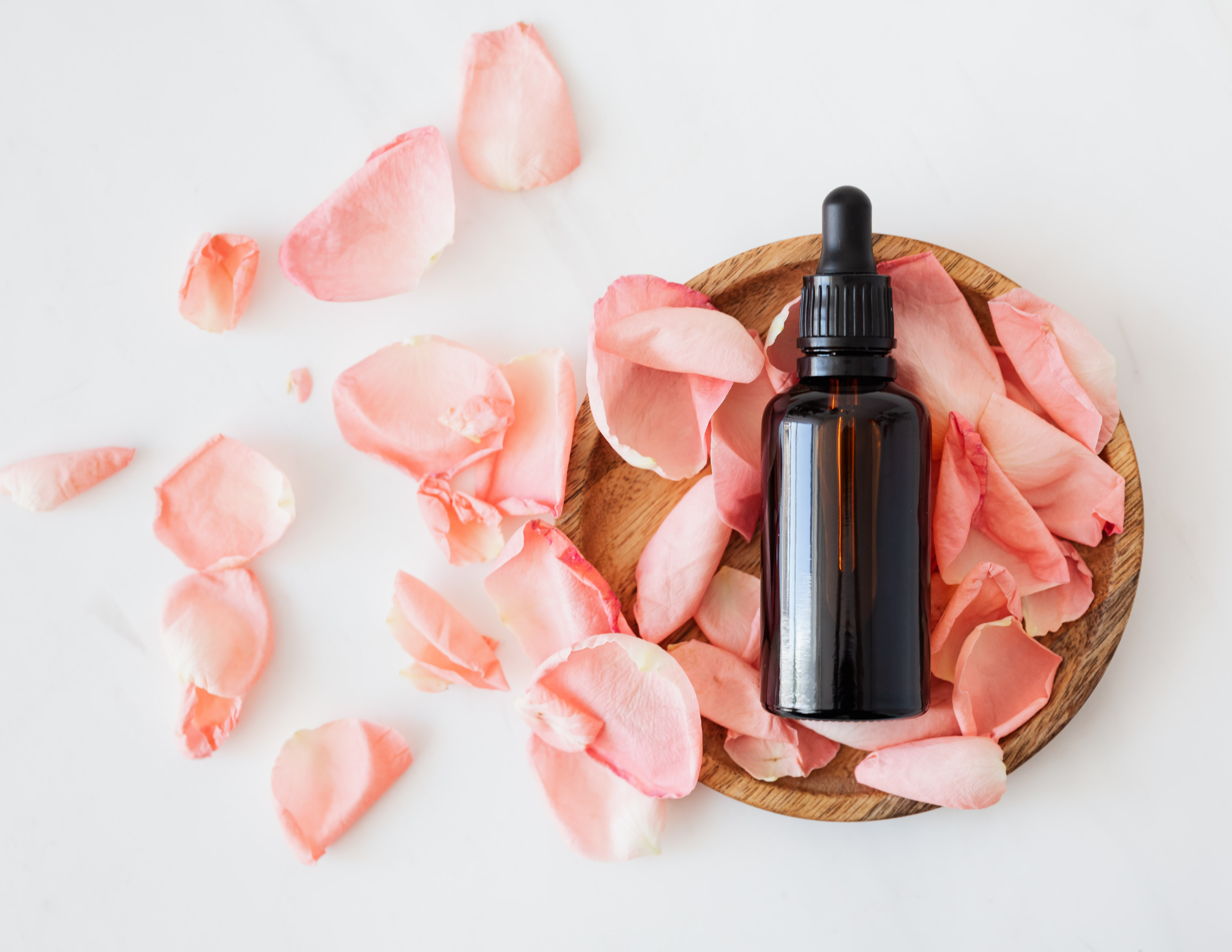 Seasonal Aromatherapy Essential oil laid atop rose petals in a textured wooden bowl and a bright white background