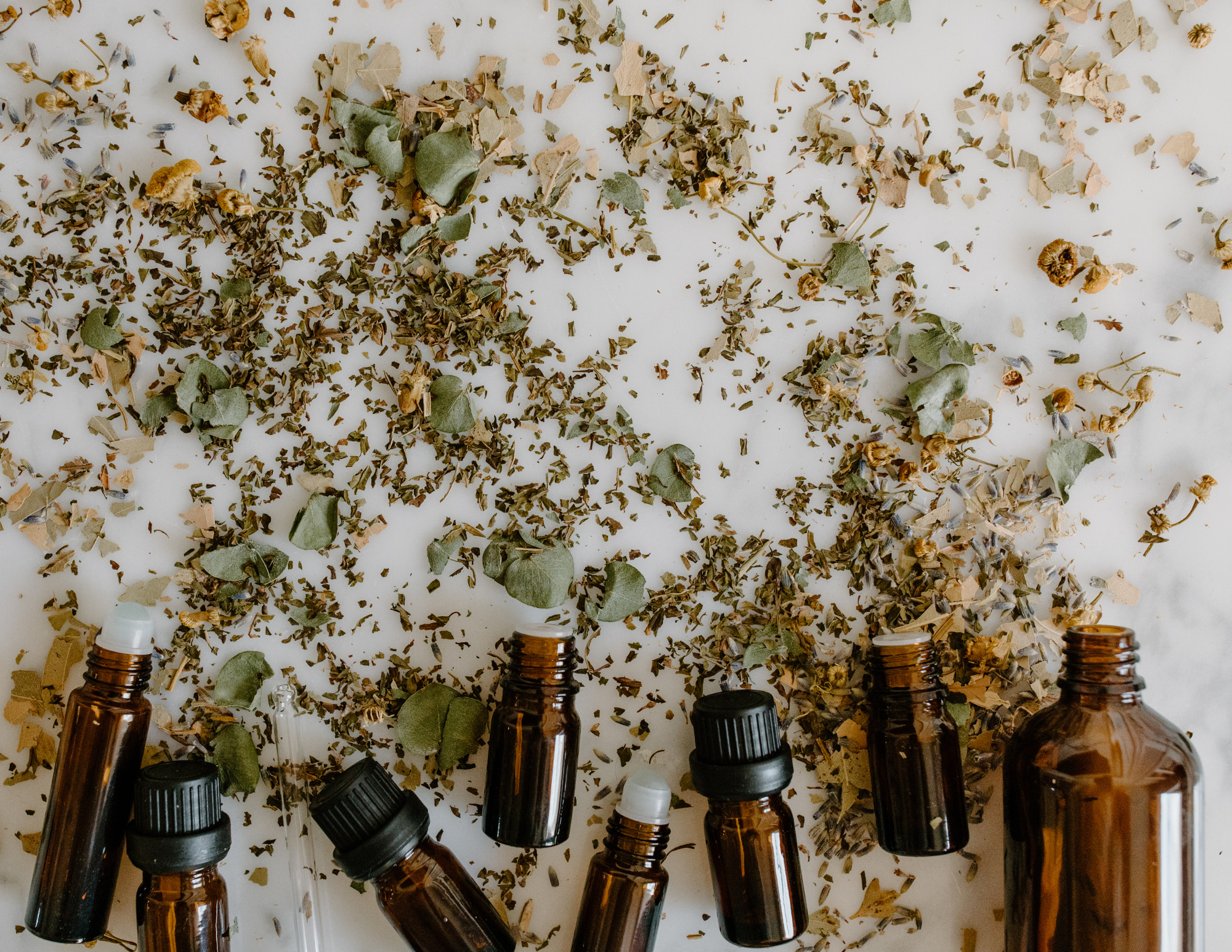 Aromatherapy Essential Oil bottles on a white table with eucalyptus leaves and aromatic herbs
