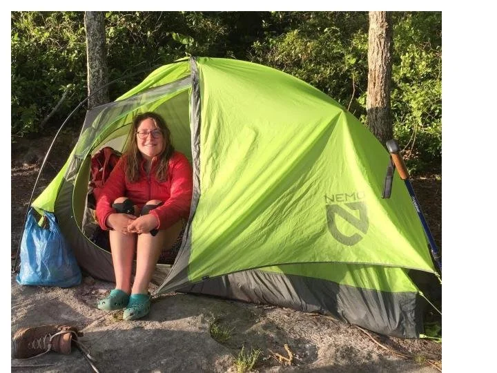 Woman smiling with glasses sitting inside a lime green camping tent in the woods