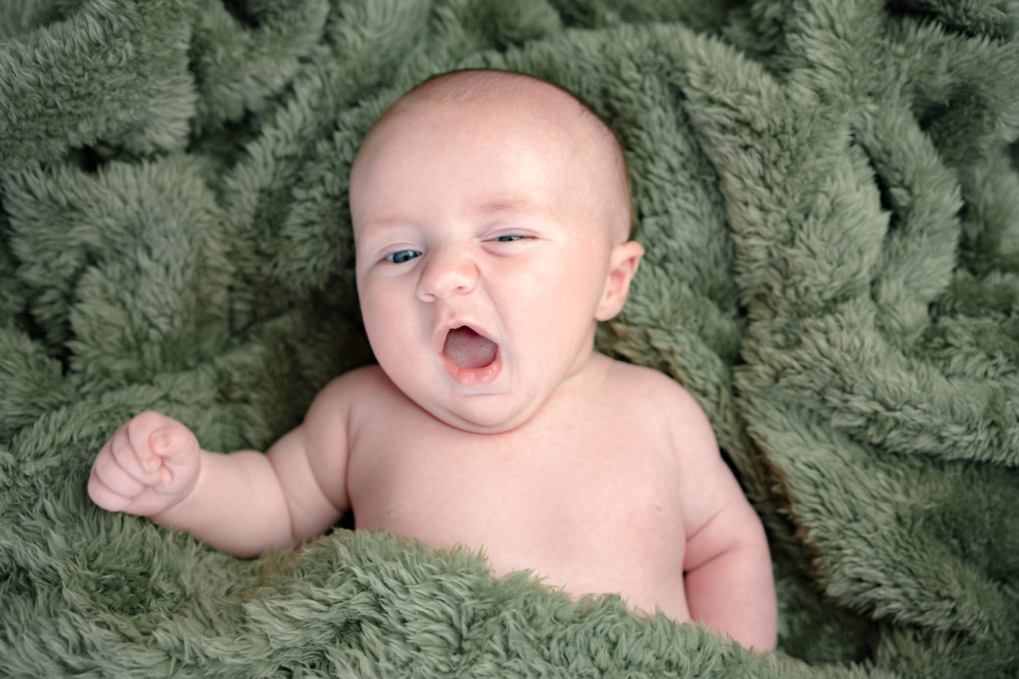A baby yawning wrapped in a green blanket.