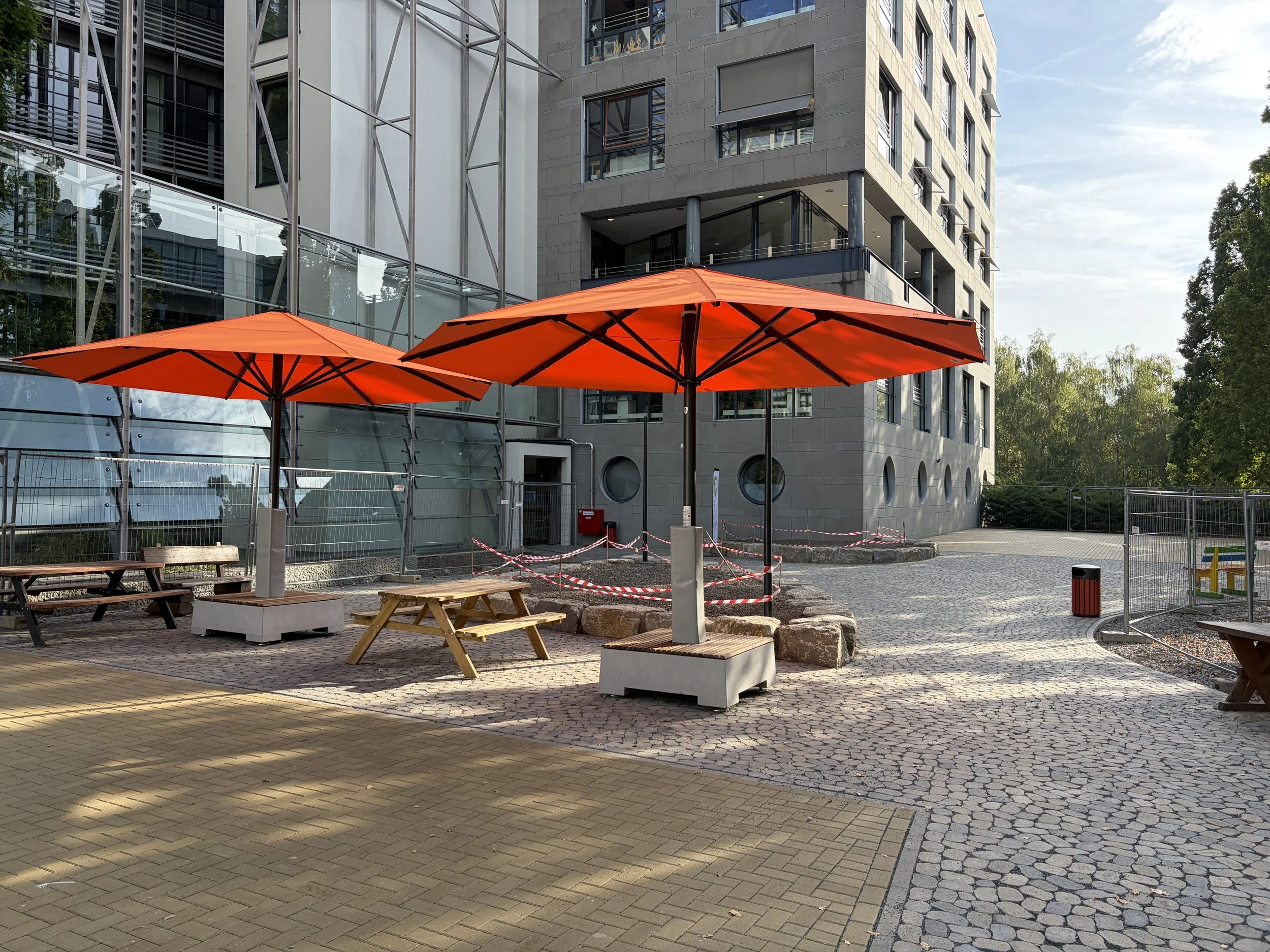 Realisierung im Eiltempo eines Teils des neuen Schulhofs für die ASB Erasmus Frankfurter Stadtschule Grundschule gGmbH bis Schulbeginn 10.8.2026. Bunte Sonnenschirme stehen auf dem von uns sehr geschätzten Arena-Pflaster.