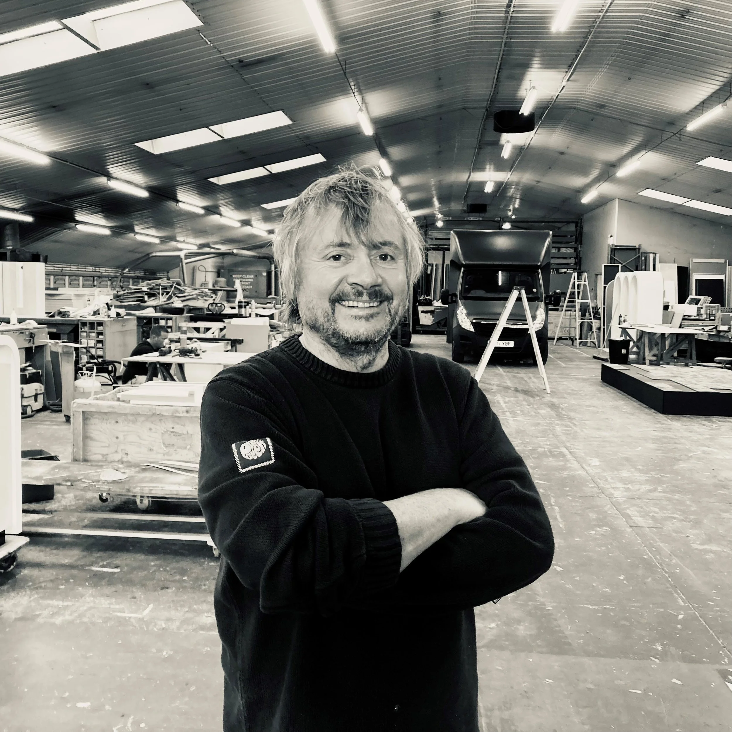 Creator International's Director smiling with arms crossed in our scenic set build workshop, surrounded by fabrication tools and equipment