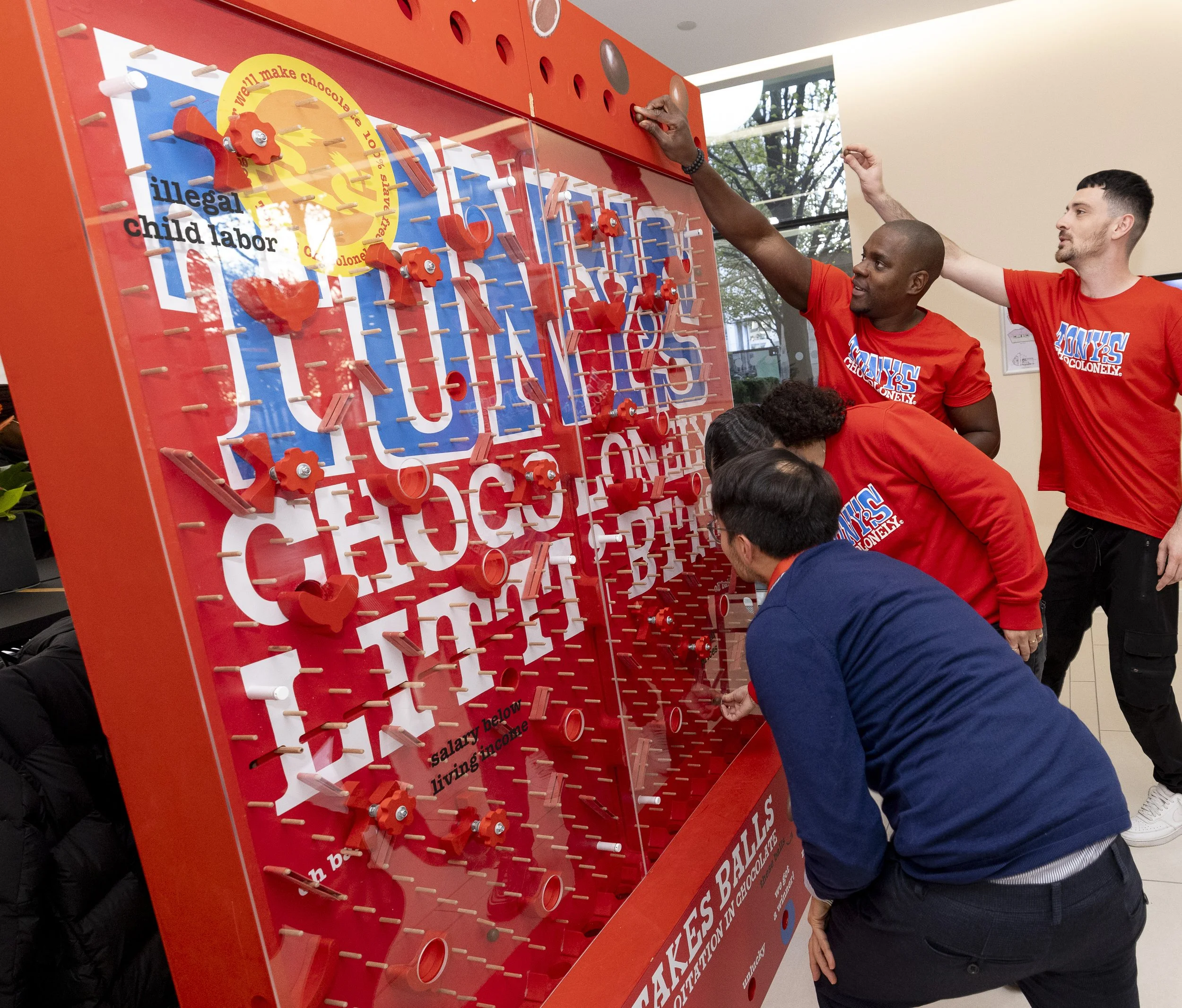 Group of people playing a red plinko-style game about chocolate and labor issues.