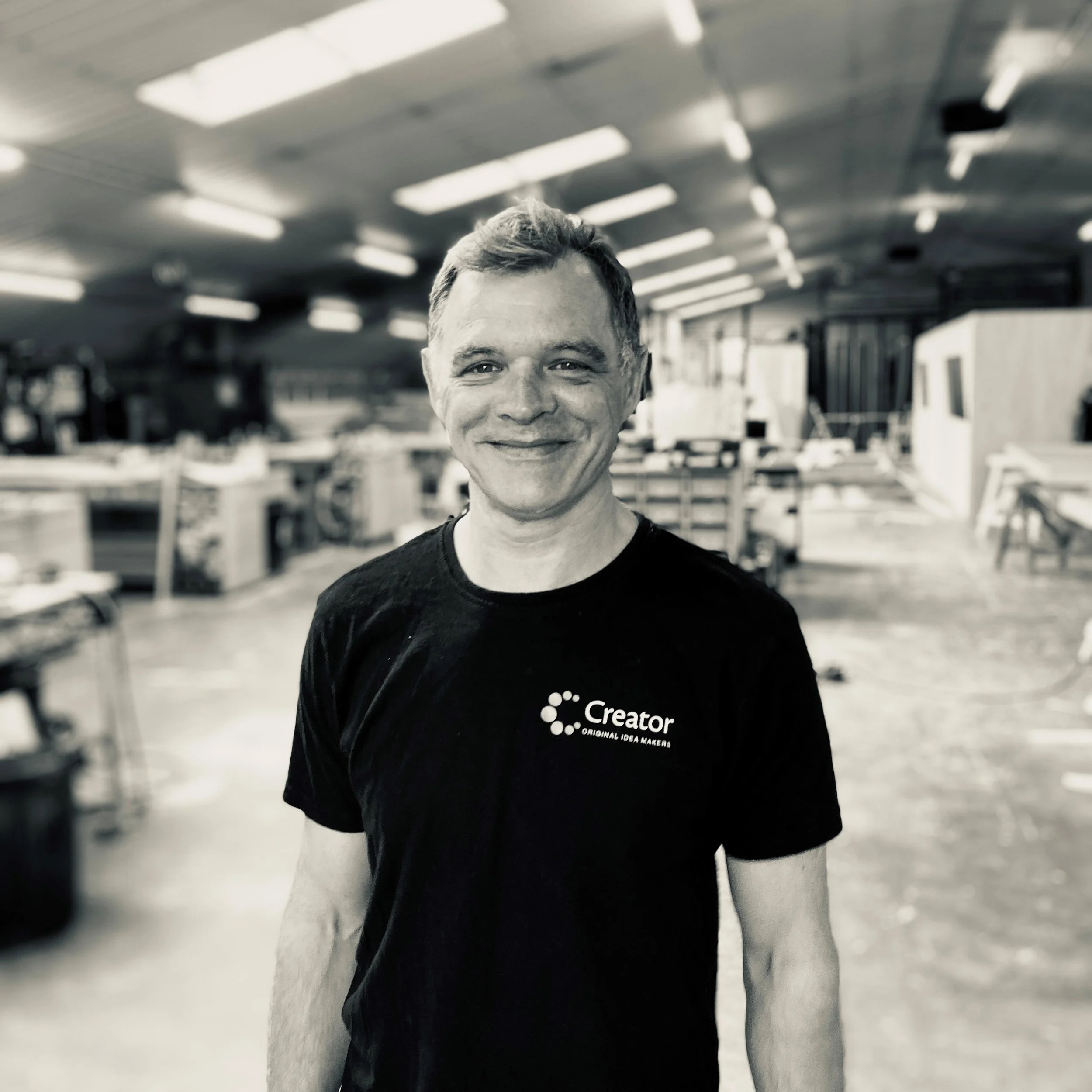 CNC operator and CAD designer in a workshop wearing a black t-shirt with the word 'Creator' printed on it.