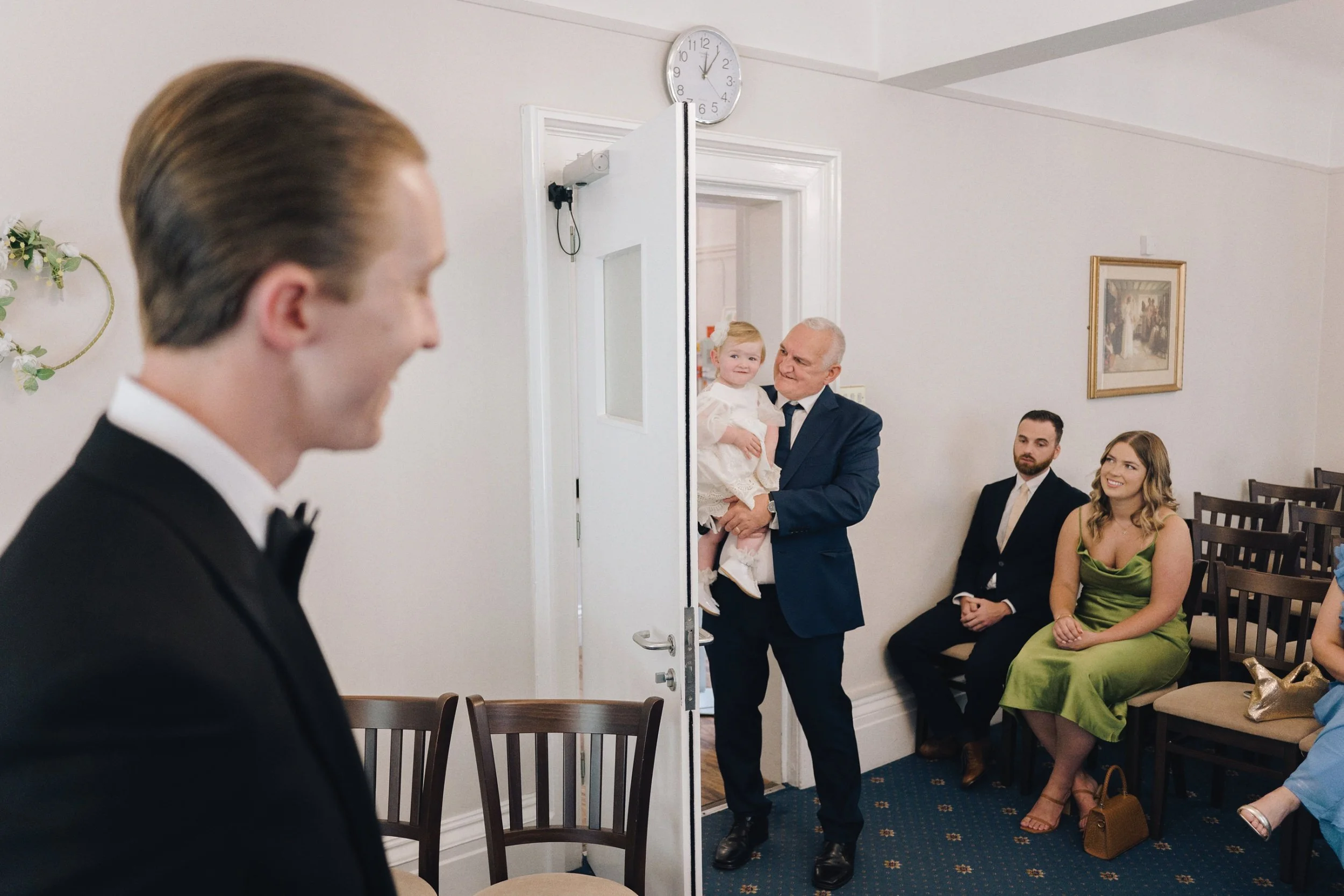 Groom smiles at his wedding guests as he waits for the bride to enter the ceremony room