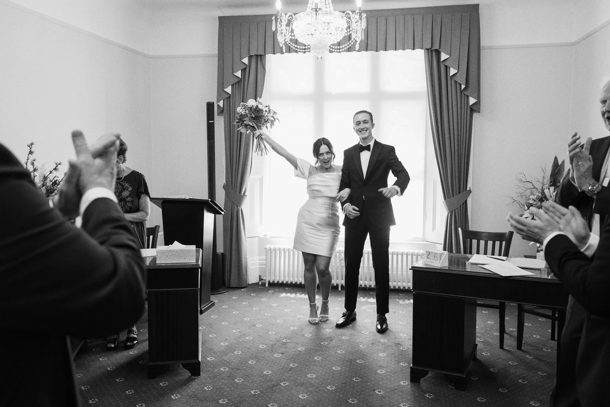 Bride holds her bridal bouquet in the air as her and her new husband walk out of their wedding ceremony in Guildford