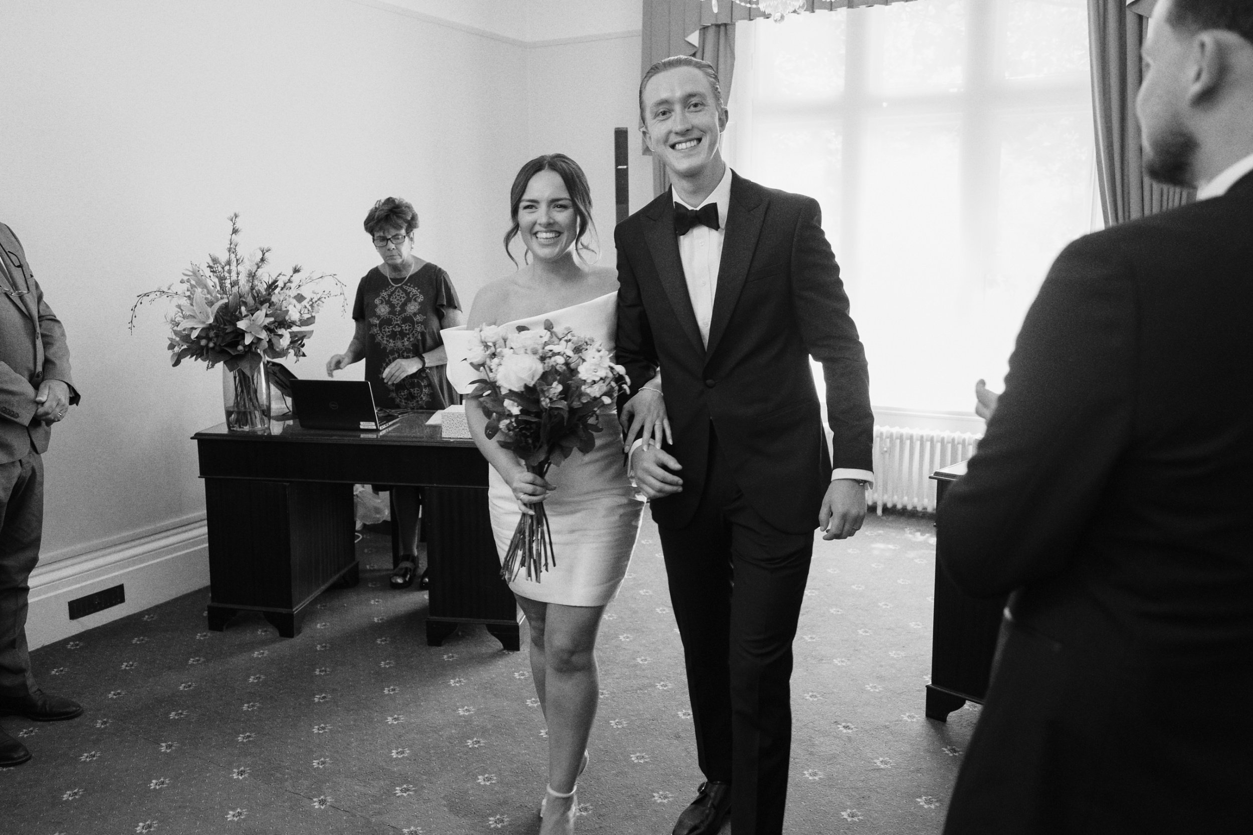 Bride and groom smile at the wedding photographer as they leave their wedding venue in Guildford, Surrey