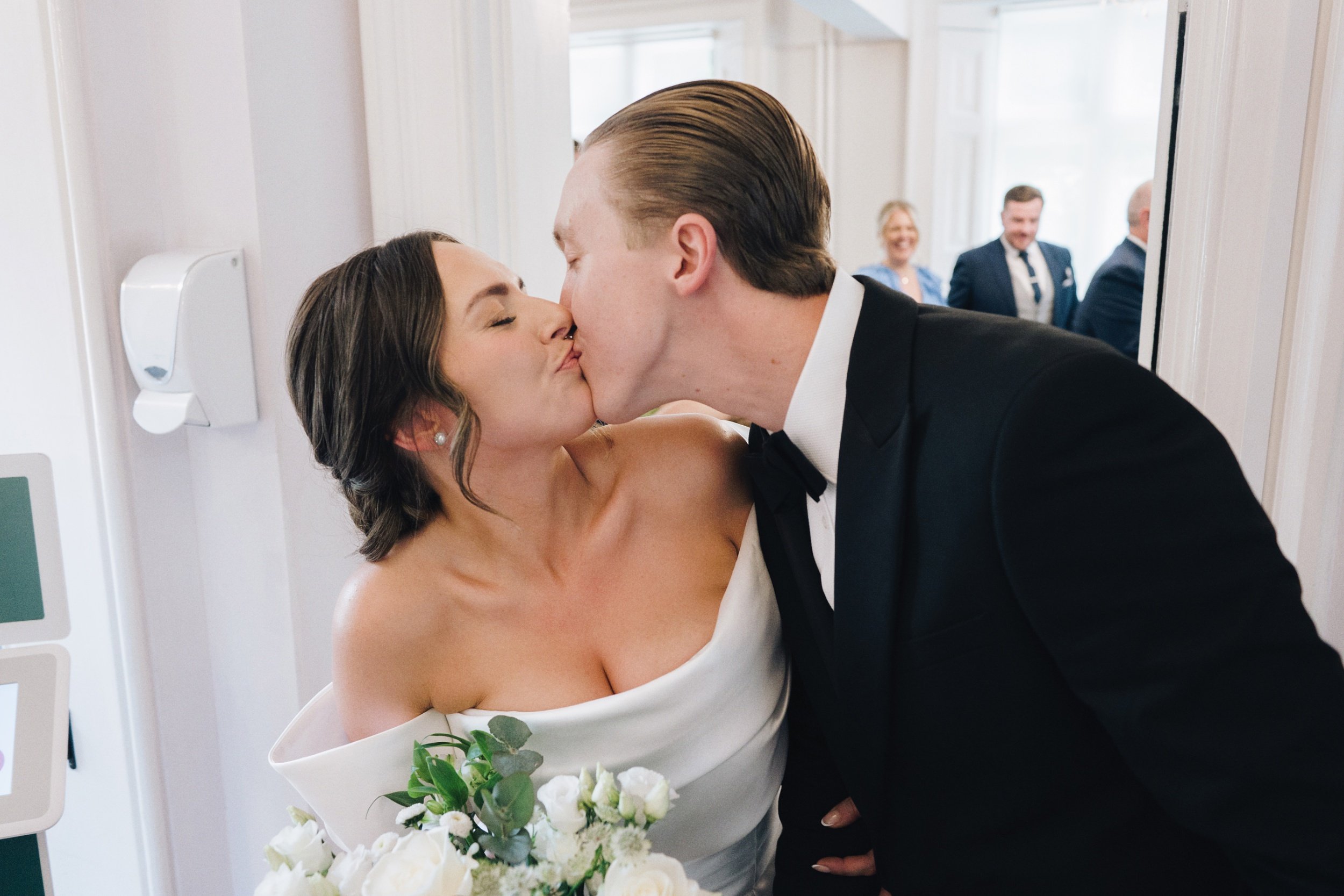 Bride and groom share a kiss as they walk out of their wedding venue in Guildford as newlyweds