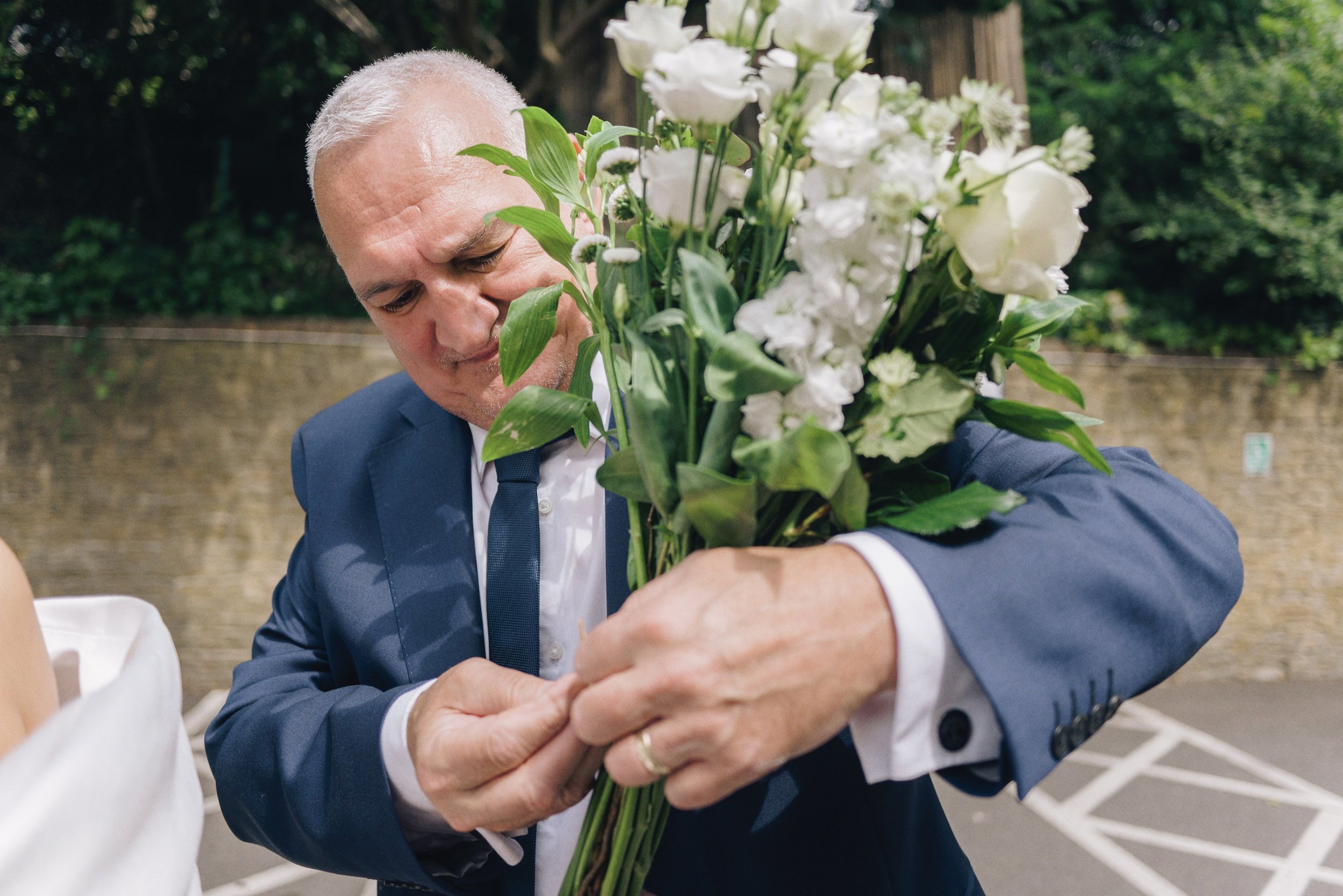 Father of the bride tying the bridal bouquet outside the wedding venue in Guildford