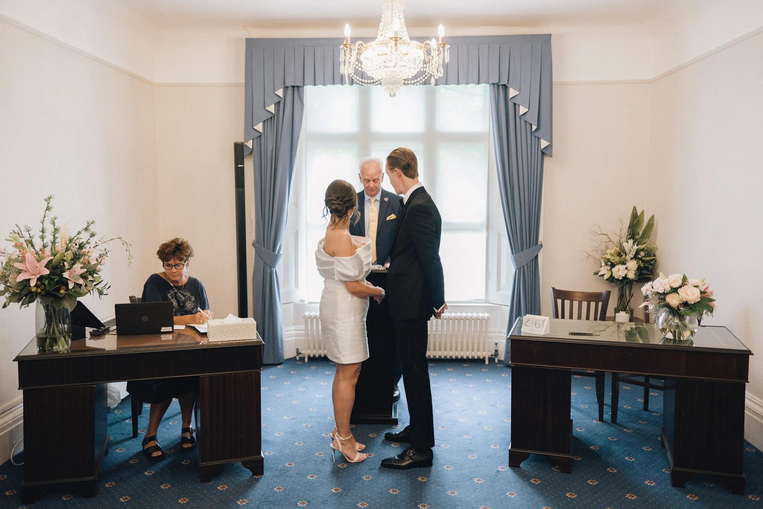 Bride and groom hold hands while they listen to the registrar at Guildford Register Office