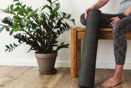 Frau mit Yogamatte sitzt auf einer Bank neben ihr ist eine Blume