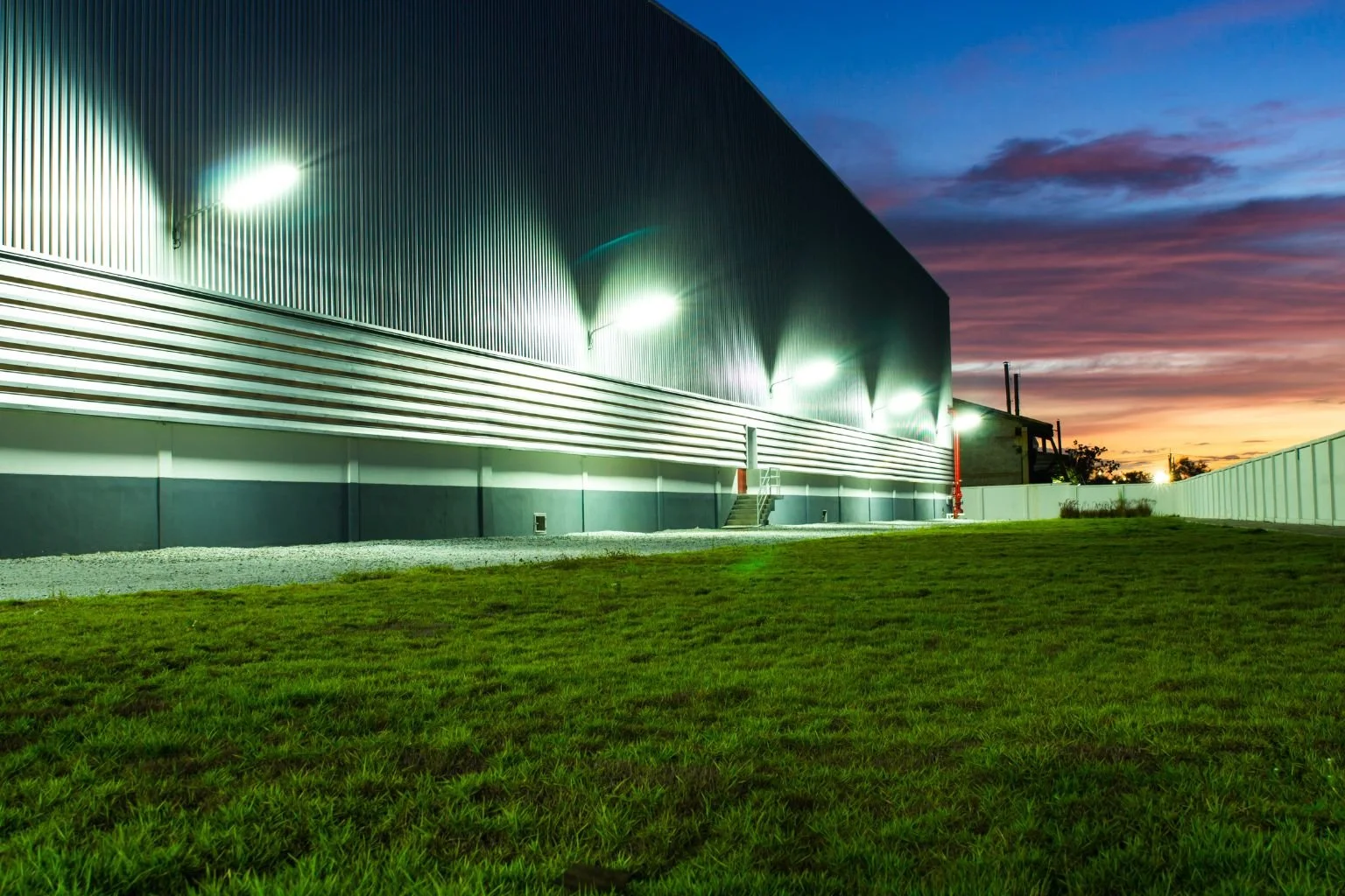 Powerful exterior LED building lights illuminate the side of a large warehouse at dusk, professionally installed by an Apple Valley electrician.
