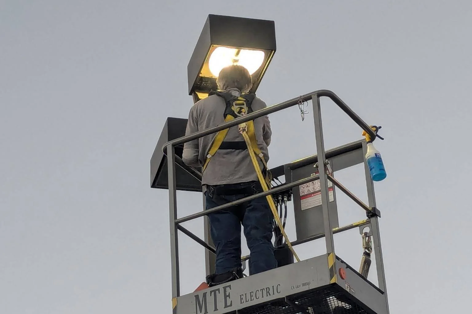 MTE Electric electrician performing an LED parking lot lighting conversion from a boom lift at Family Medical Center in Phelan, California by bypassing the existing metal halide ballast and installing an LED replacement lamp.