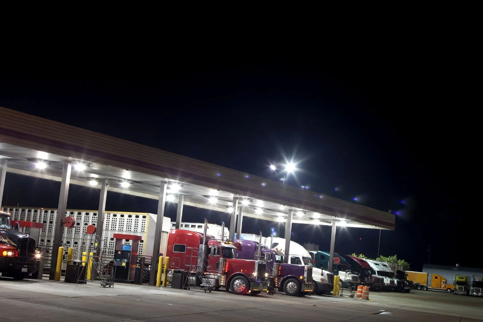 A row of semi-trucks parked at night under bright, professional canopy lighting installed by an Apple Valley electrician.