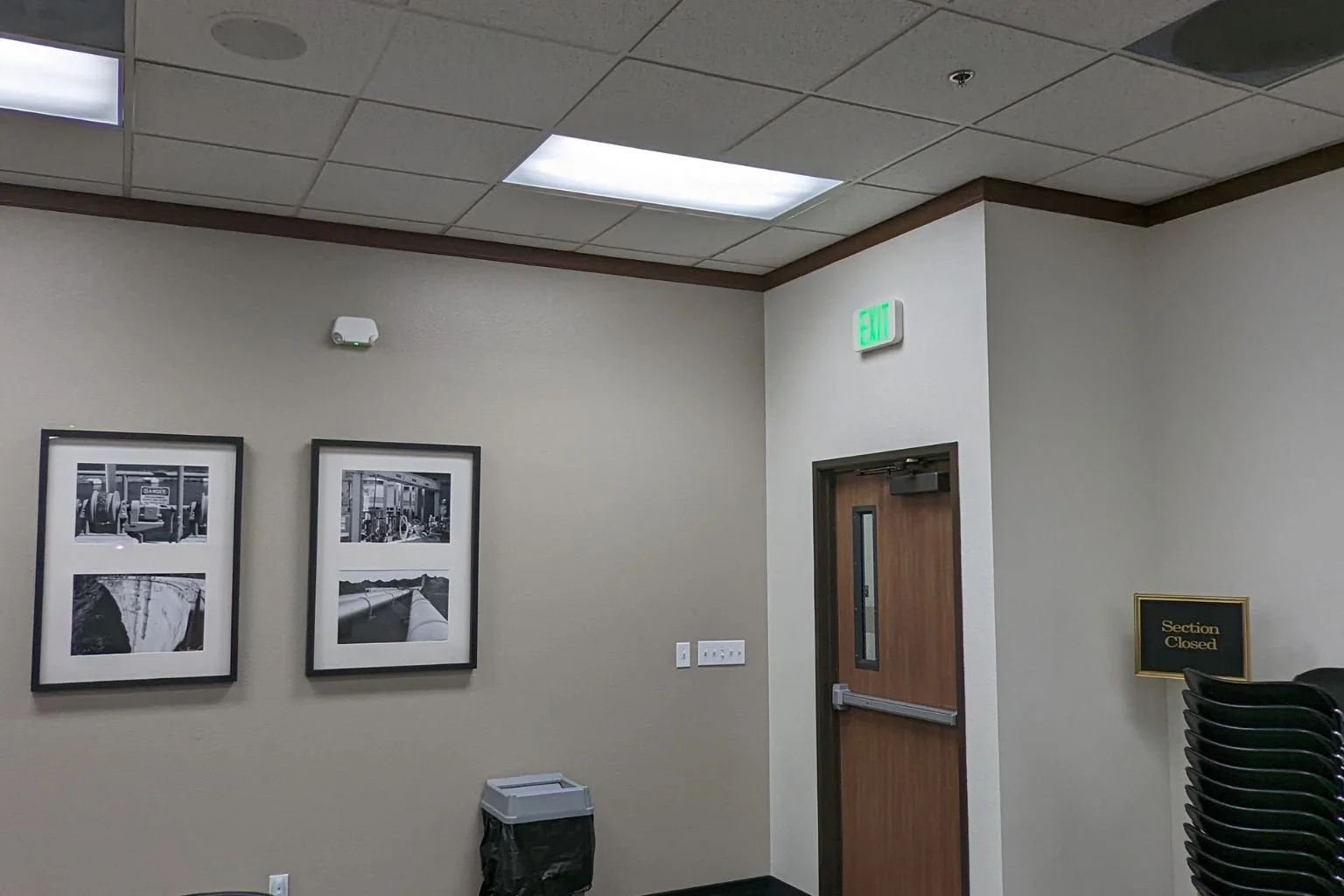 Illuminated green LED exit sign mounted above a wood-frame glass door inside a clean, modern commercial office building.