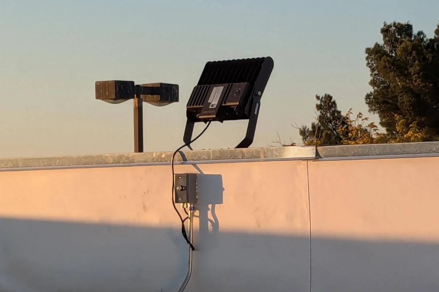Electrical conduit and rooftop wiring installed on conduit supports for a new LED flood light at Cycle Gear in Victorville, California, providing reliable power for exterior parking lot lighting.