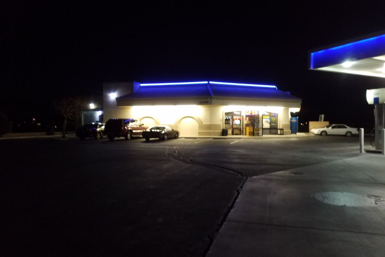 Wide view of Chevron gas station in Apple Valley with blue LED roofline lighting illuminating the building and parking lot at night.
