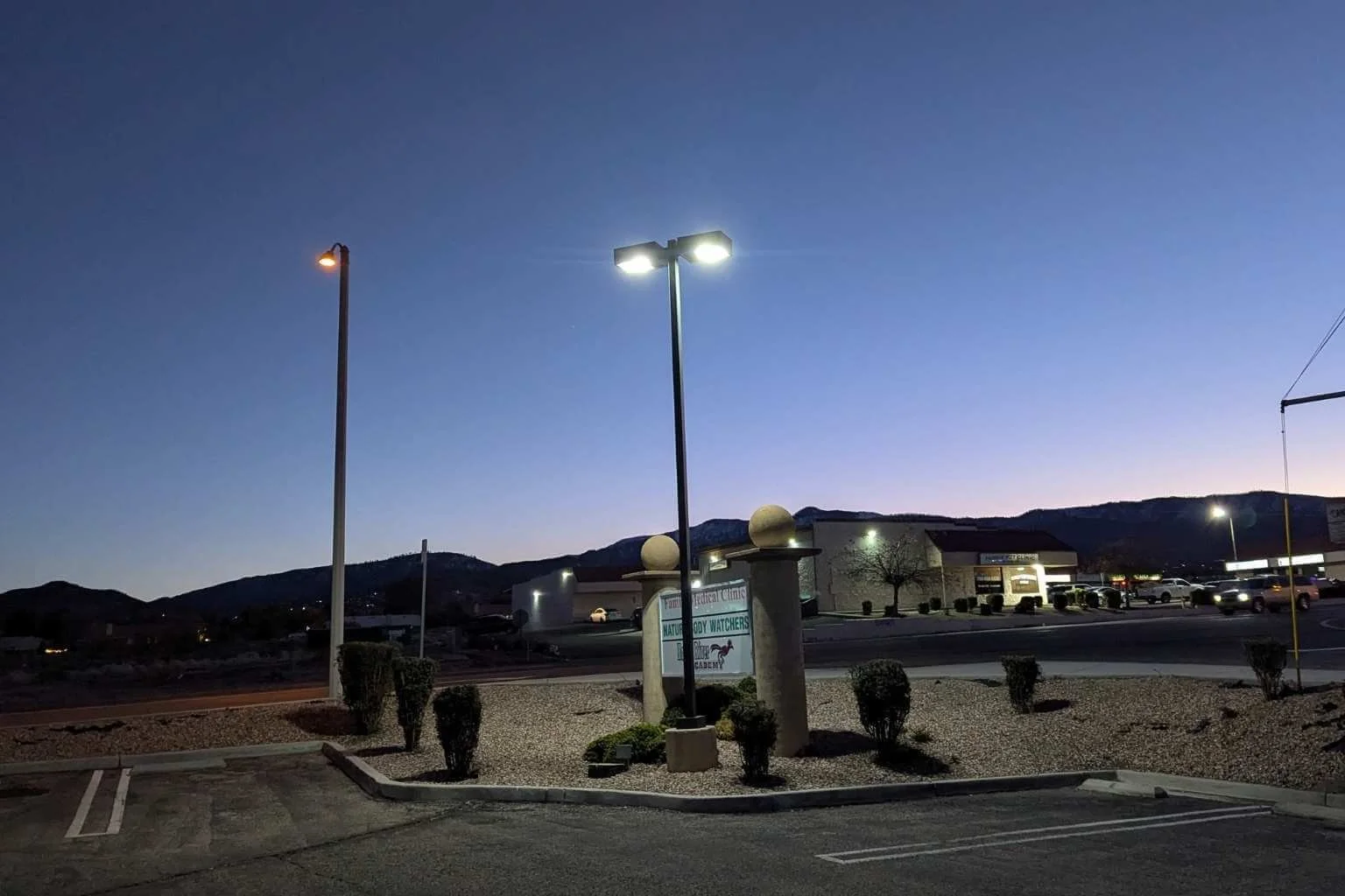 Completed LED parking lot lighting conversion at Family Medical Center in Phelan, California, showing bright white LED fixtures illuminating the parking lot while an older metal halide fixture remains visible in the background.