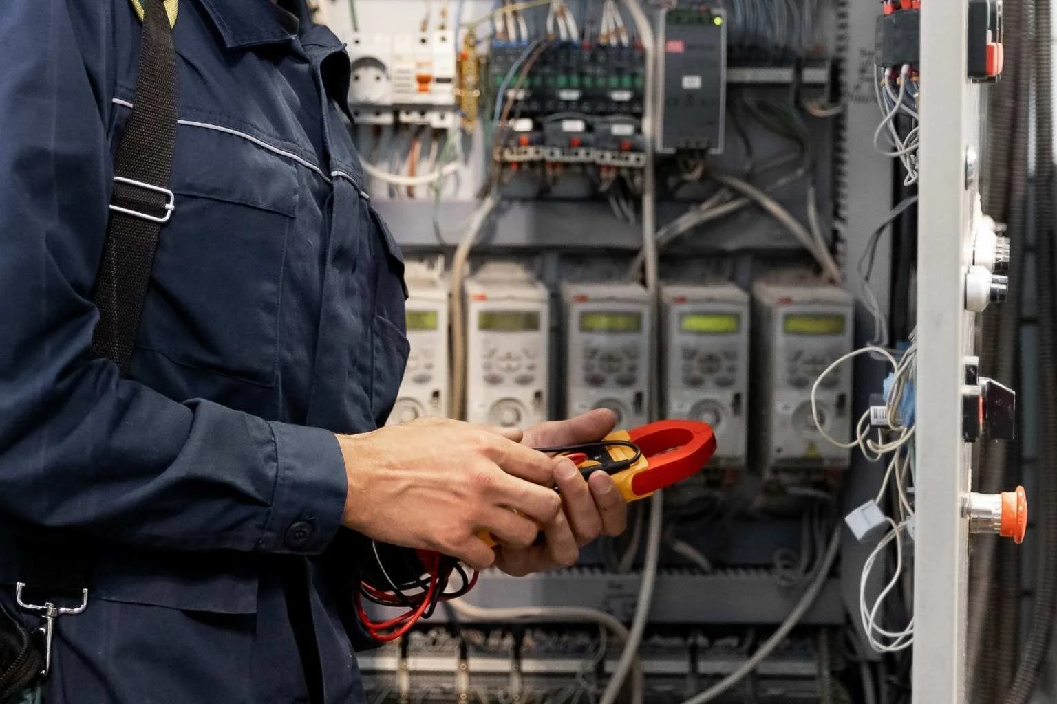 Commercial electrical services technician using a clamp meter to test and troubleshoot wiring inside an electrical panel for a commercial building.