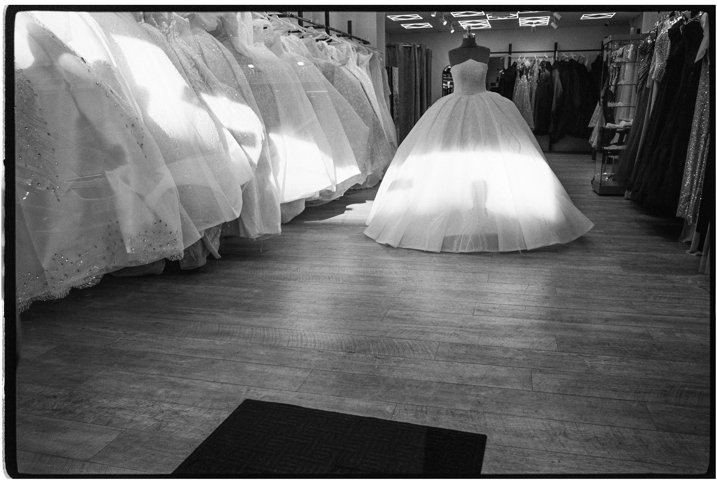 Black and white photo of a bridal store with a display of wedding dresses on mannequins and racks.